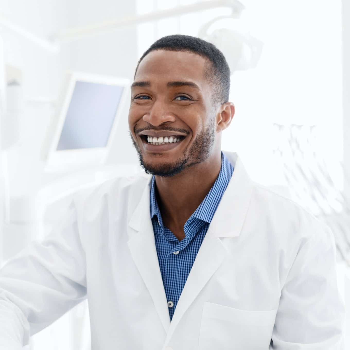 Handsome black dentist smiling over modern dental clinic background